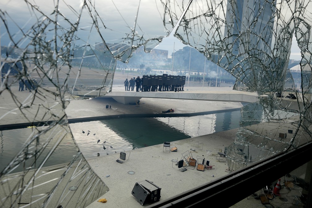 Policiais sobem a rampa do Palácio do Planalto vistos através de uma janela quebrada por vândalos durante invasão em Brasília — Foto: Eraldo Peres/AP